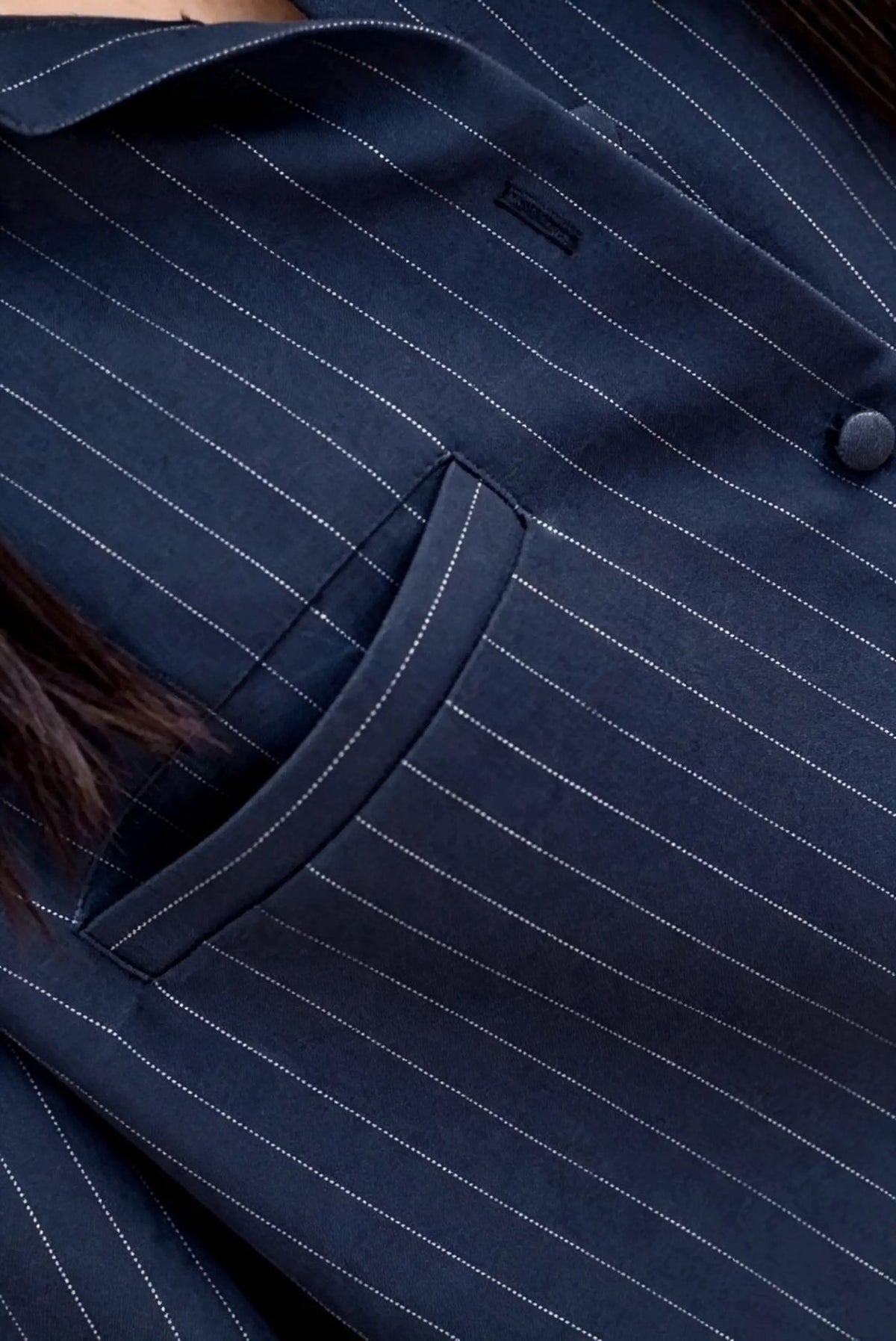 Close-up of a navy blue pinstripe blazer with thin white vertical stripes, showing a pocket and button detail.