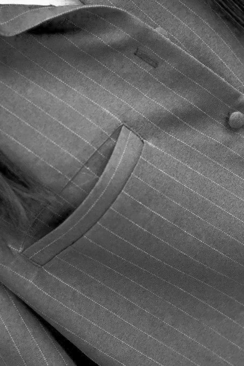 Close-up of a gray pinstripe suit jacket showing the fabric texture, a button, and a pocket.
