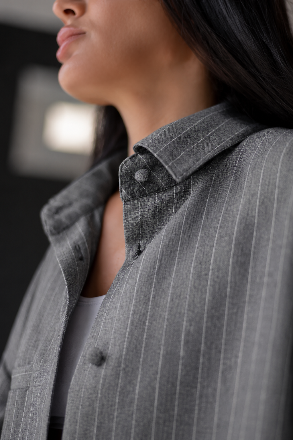 Close-up of a person wearing a gray pinstriped button-up shirt jacket, showing the collar, button, and fabric texture.